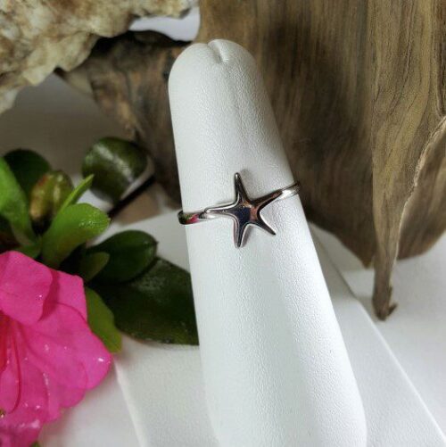 Silver starfish ring displayed on a white stand with a pink flower nearby.