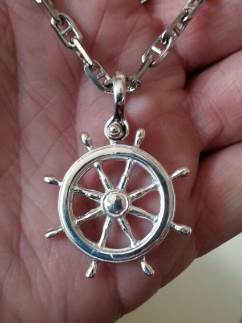 Silver ship wheel pendant necklace held in hand.