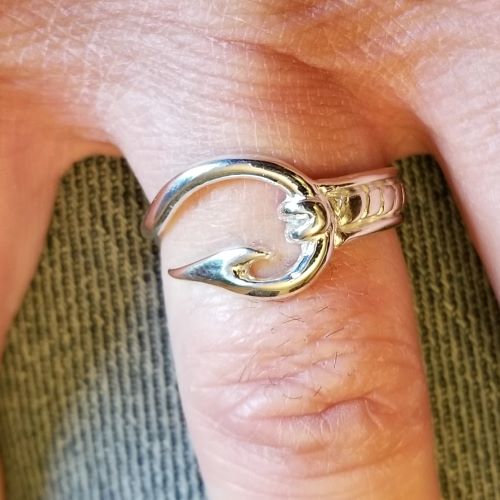 A silver ring shaped like a fish on a finger.