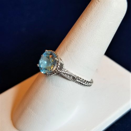 Elegant silver ring with a light blue gemstone and intricate band design.
