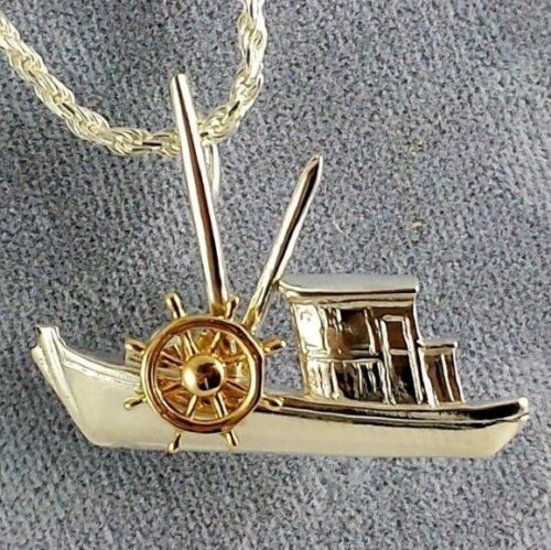 A gold and silver boat pendant with a chain on a textured surface.