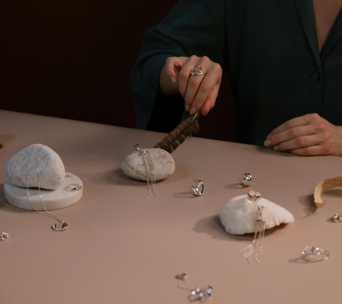 Hands delicately arranging white stones and small objects on a pink surface.