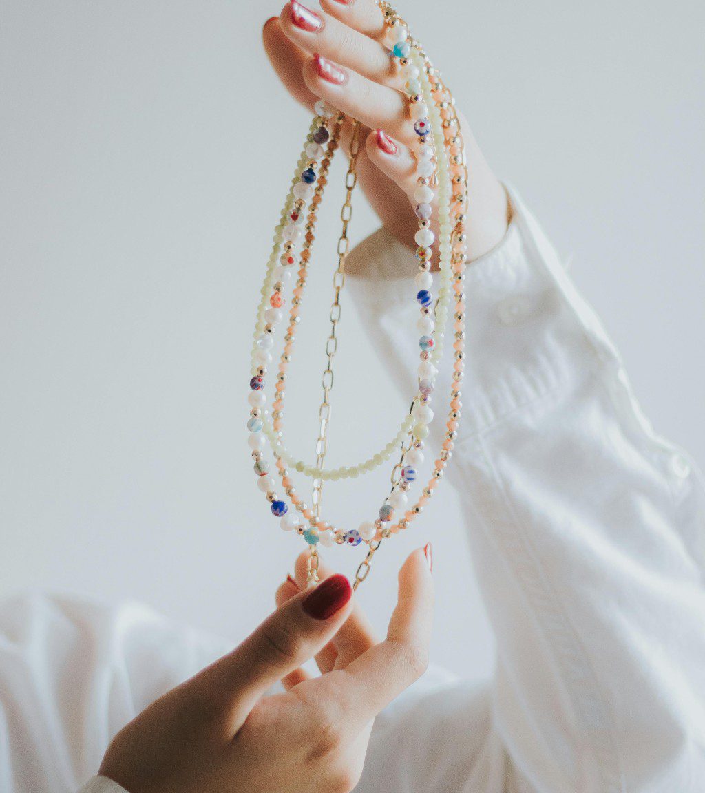 Hands holding delicate beaded necklaces against a soft background.