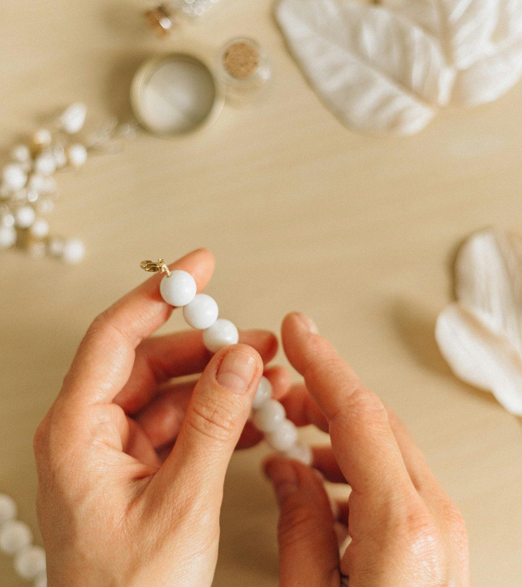 Hands holding a delicate beaded necklace with a white feather in the background.
